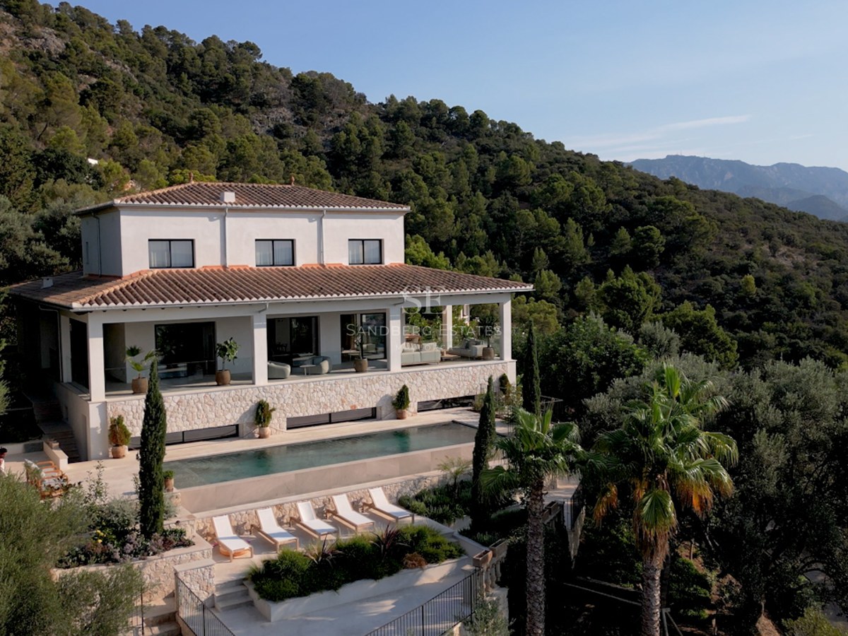 Erhöhte Ansicht einer weißen Villa mit Pool, Sonnenliegen und üppiger grüner Berglandschaft im Hintergrund.
