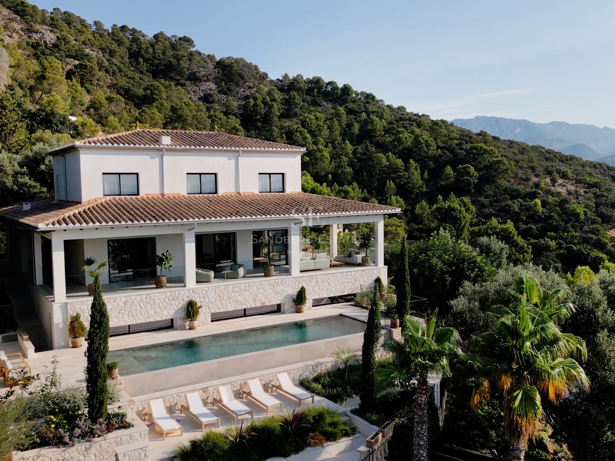 Luftaufnahme einer weißen zweistöckigen Luxusvilla mit Pool, Steinterrasse und üppiger Bergkulisse.