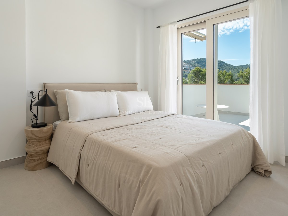 Dormitorio moderno con ropa de cama beige y puerta de cristal hacia un balcón privado con vistas a la montaña.