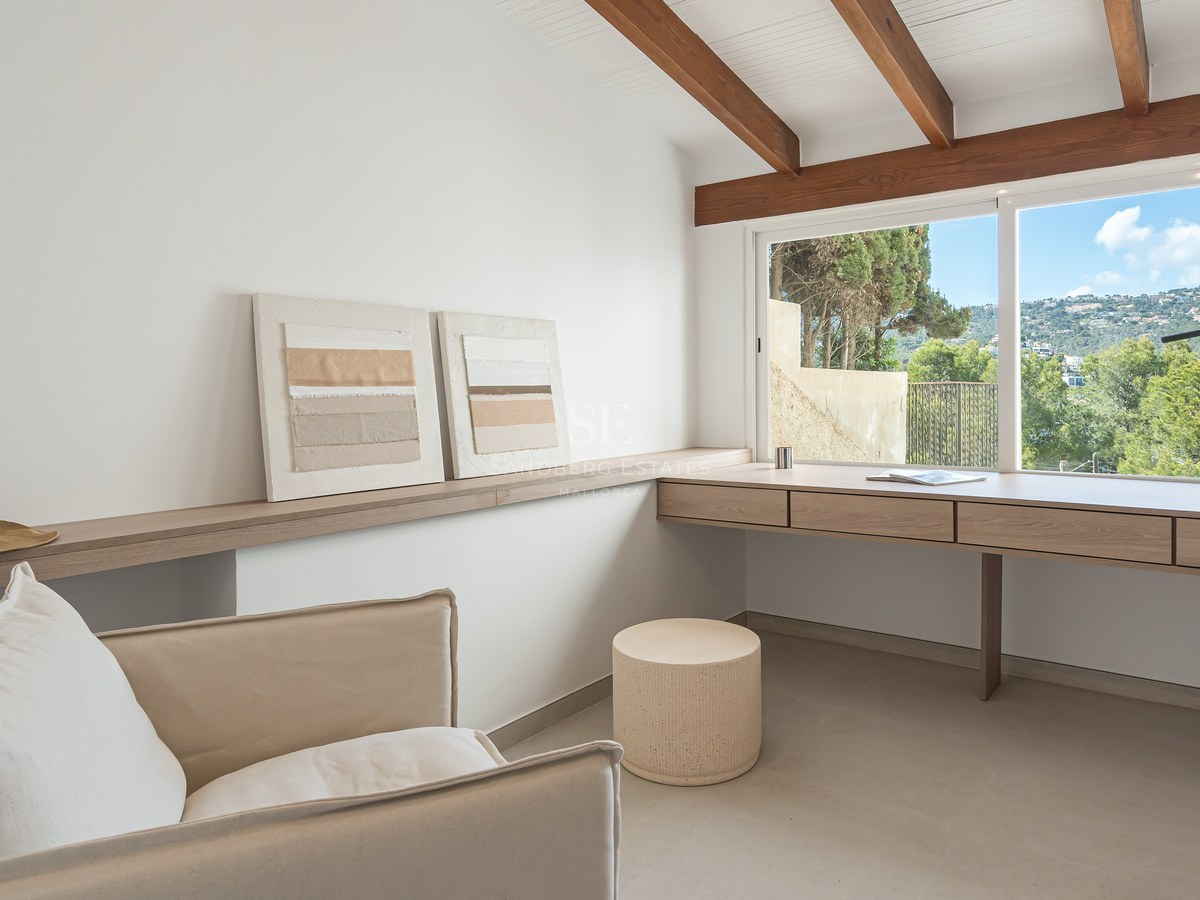 Oficina luminosa con escritorio de roble integrado, vigas de madera a la vista y ventana con vistas a la vegetación.