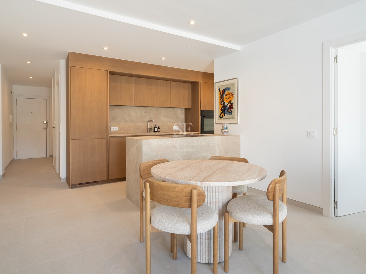 Cocina contemporánea con armarios de roble claro, isla de mármol y mesa circular de piedra con sillas de madera.