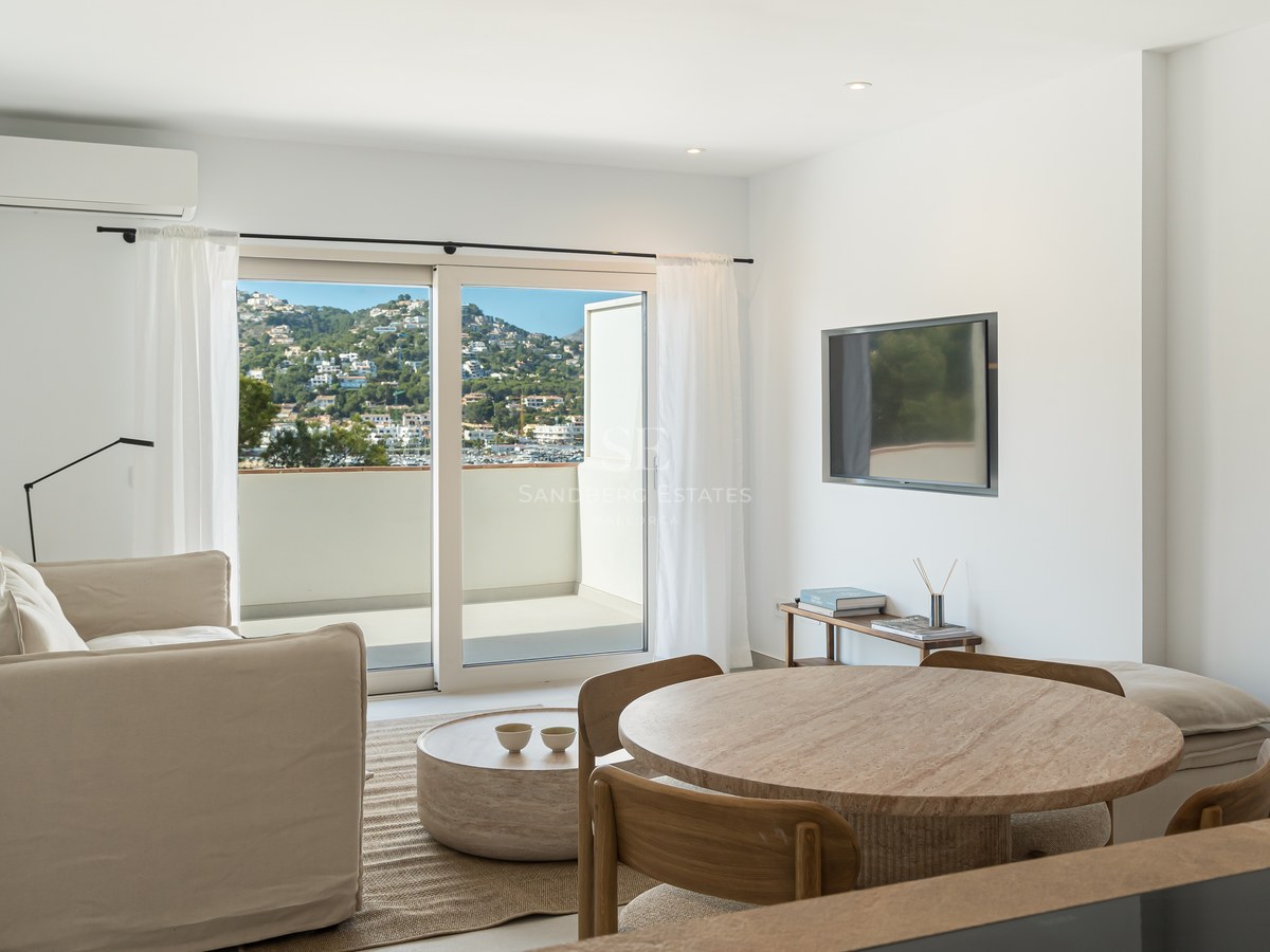 Salón moderno con muebles de madera clara y puertas correderas de cristal que dan a una terraza con vistas al puerto.
