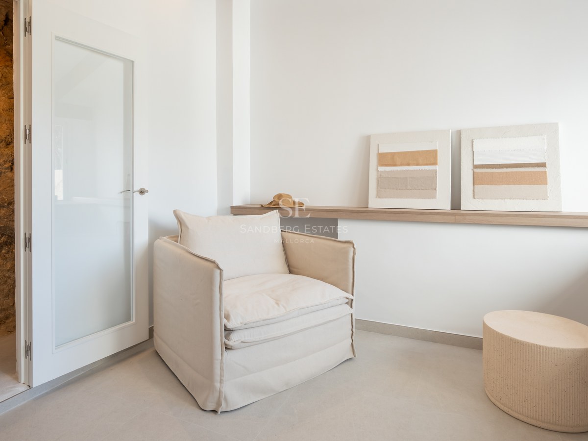 Sillón de lino beige junto a una estantería de madera clara con cuadros abstractos en una habitación luminosa.