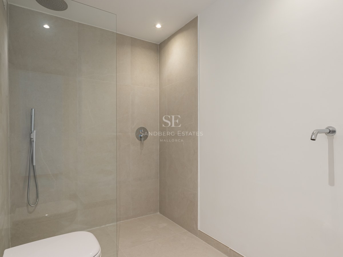 Ducha moderna con mampara de cristal, azulejos beige de gran formato y grifería de cromo empotrada.