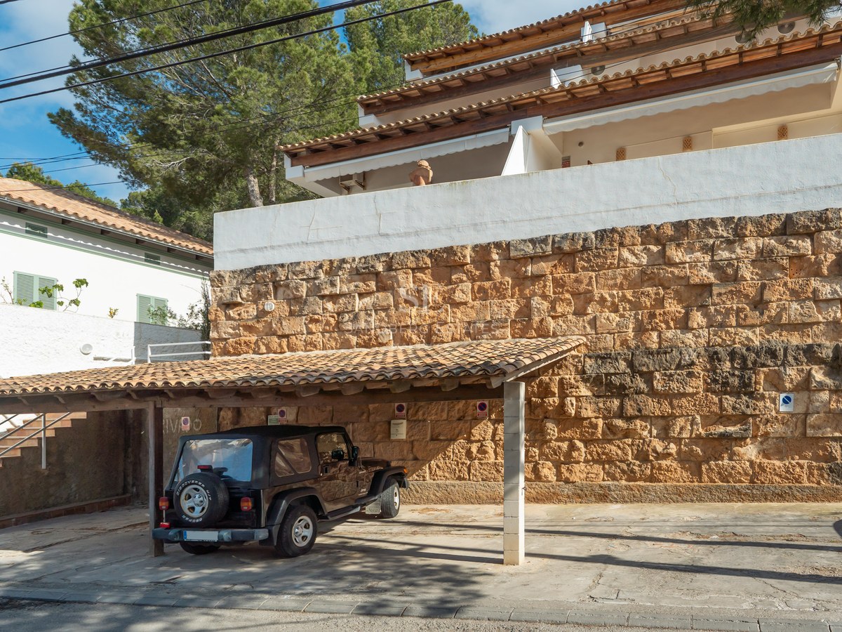 Vehículo todoterreno negro bajo un aparcamiento cubierto con techo de tejas y una robusta pared de piedra natural.