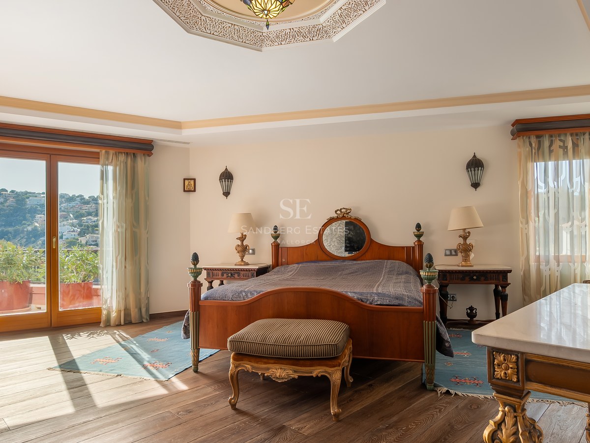 Chambre de style traditionnel avec un lit en bois, plafond orné et porte vitrée menant à un balcon.