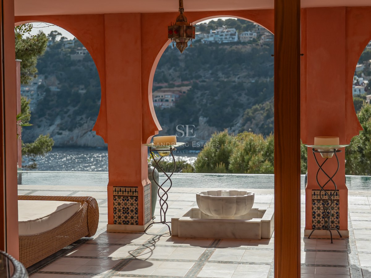 Terrasse couverte avec arches terracotta et colonnes carrelées surplombant une baie bleue et des collines vertes.