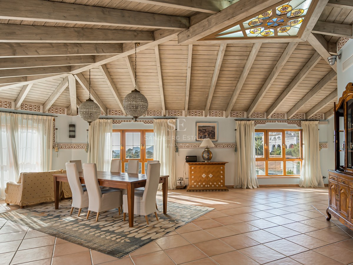 Salle à manger avec plafond voûté en bois, carreaux de terre cuite et grandes fenêtres lumineuses.