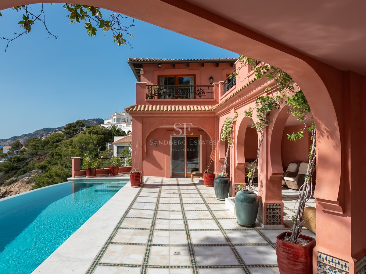 Villa de luxe aux tons terracotta avec piscine à débordement, terrasse voûtée et vue sur la côte.