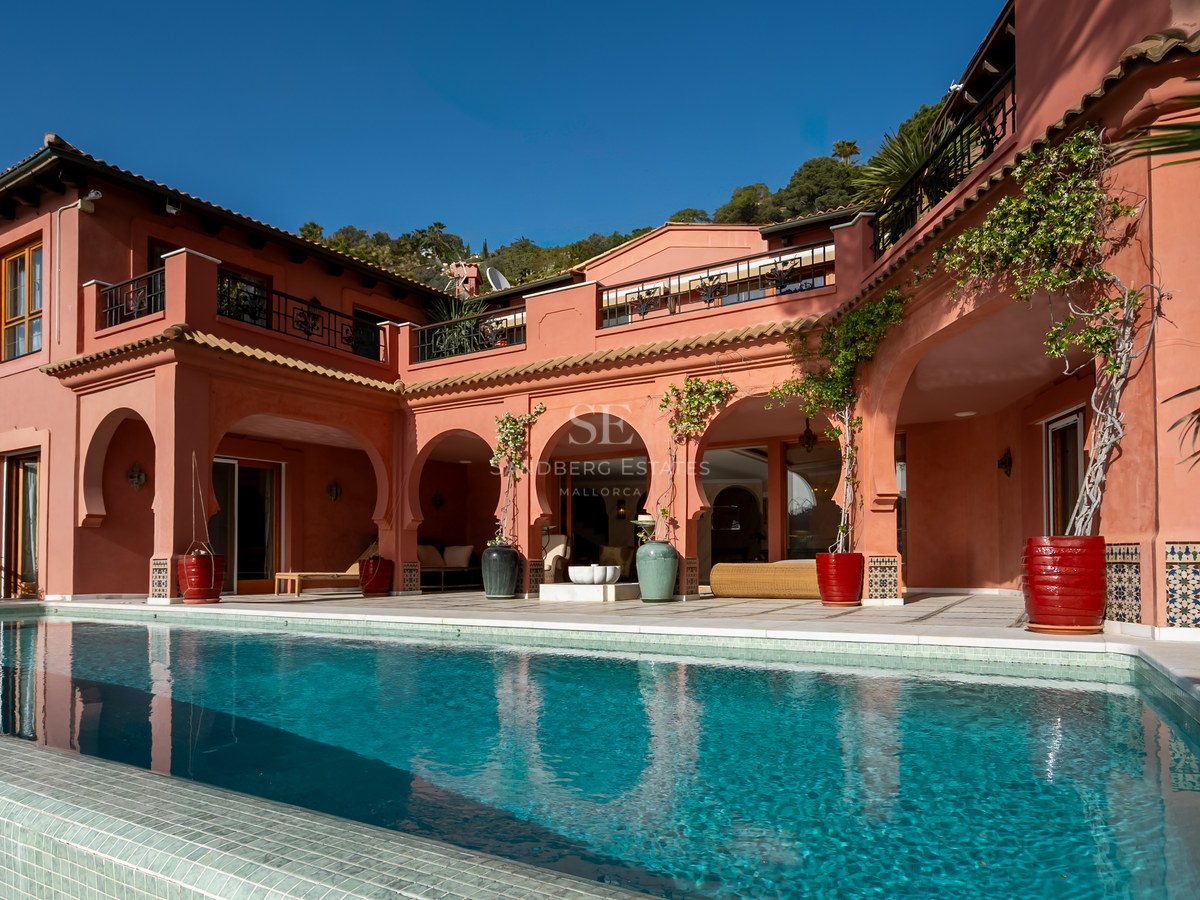 Grande piscine turquoise devant une villa terre cuite aux arches traditionnelles et terrasses ensoleillées.