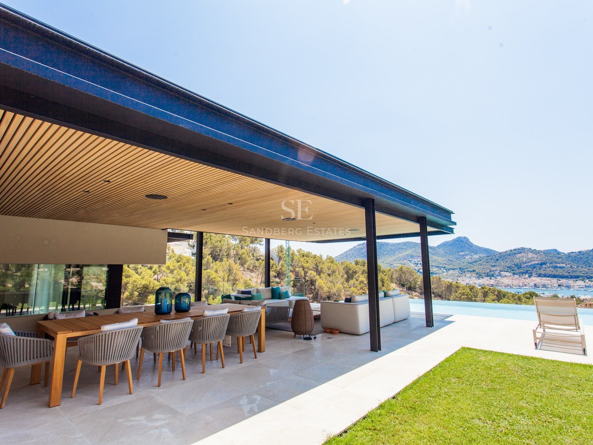 Luxuriöse Außenterrasse mit großem Holzesstisch, Lounge-Bereich und Infinity-Pool mit Blick auf die Bucht.