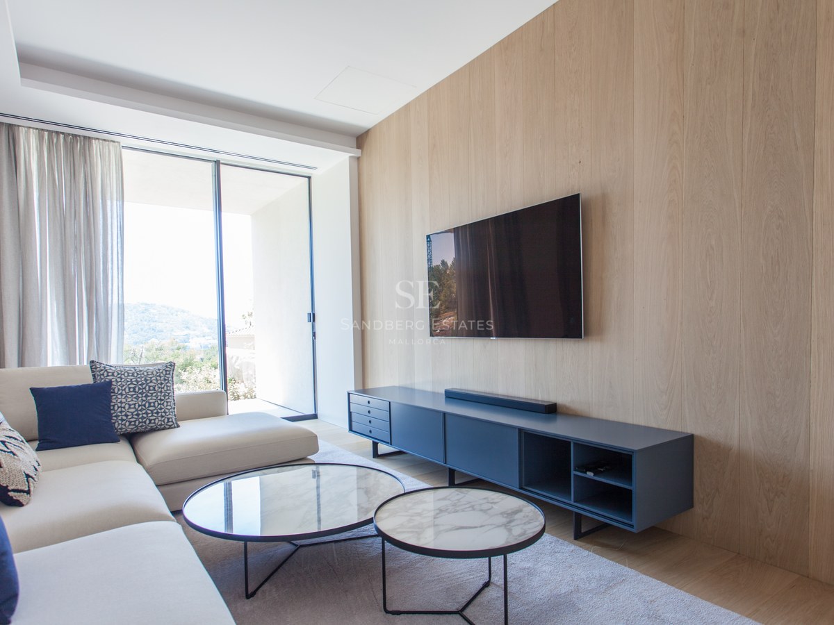 Modernes Wohnzimmer mit eichengetäfelter Wand, Wand-TV, Marmortischen und großen Fenstern mit Bergblick.