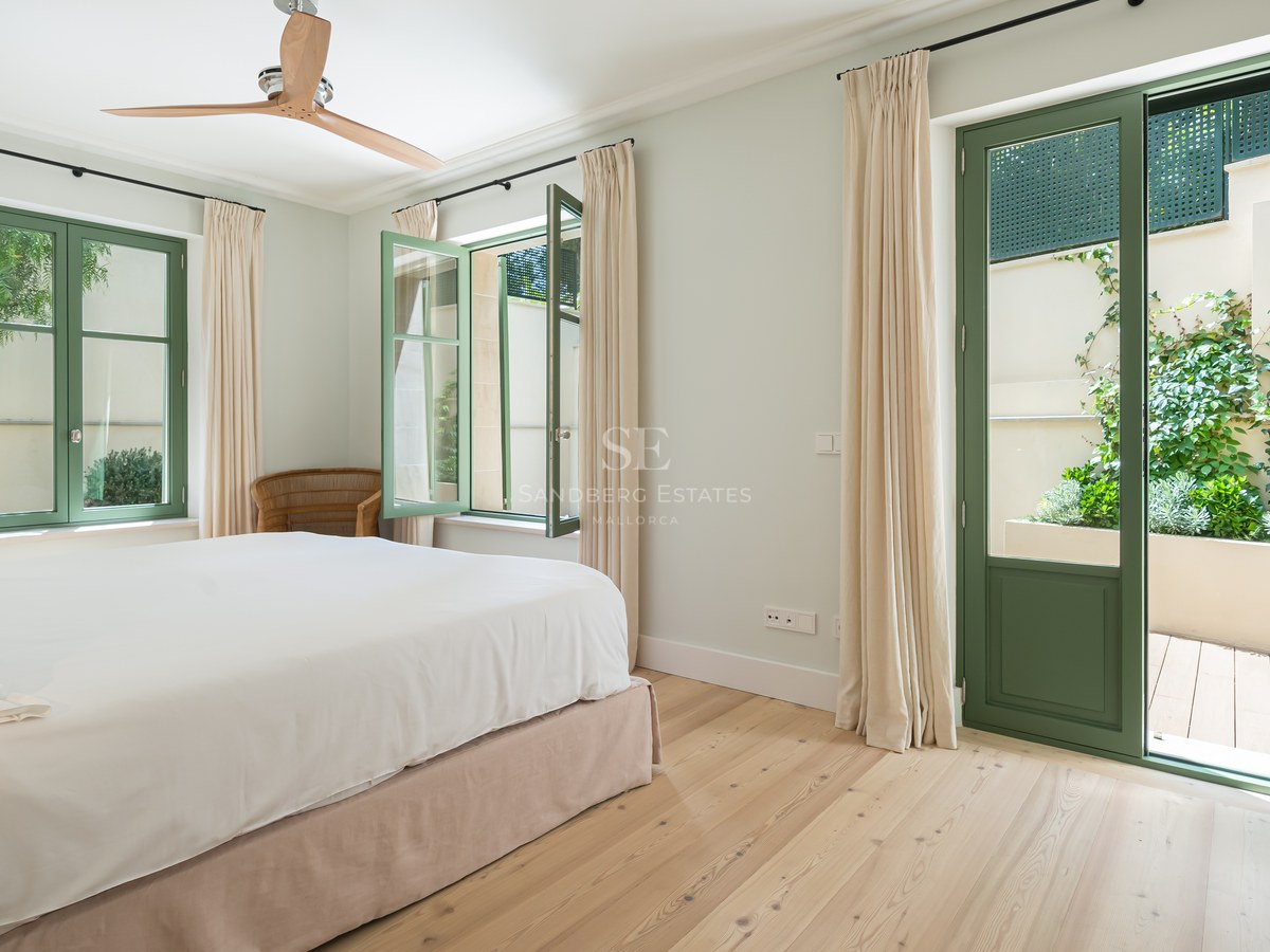 Dormitorio luminoso con suelos de madera clara, carpintería verde y acceso directo a un patio privado.