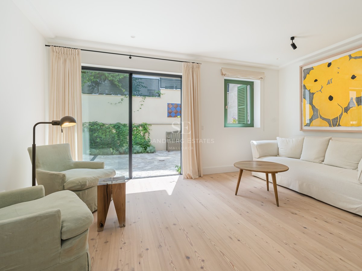 Salón moderno con suelos de roble claro, muebles en tonos crema y grandes puertas correderas de cristal hacia un patio.