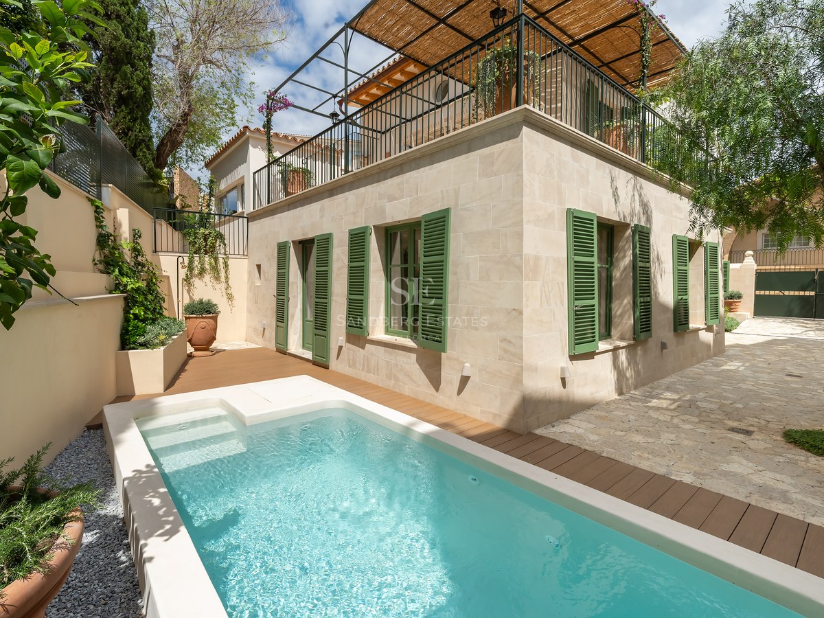 Villa de piedra con piscina turquesa, terraza de madera y persianas tradicionales verdes en Mallorca.
