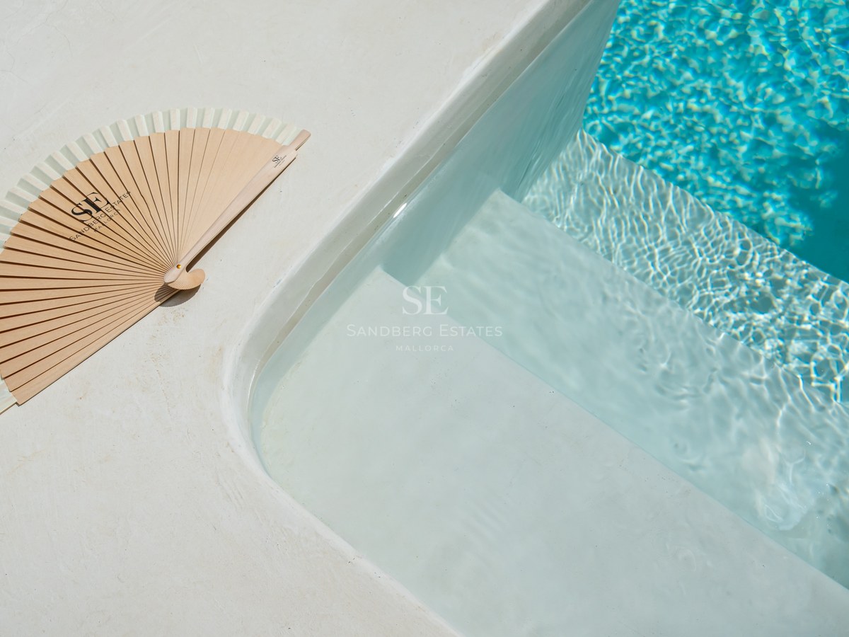 Primer plano de escalones blancos de piscina que entran en agua turquesa con un abanico de madera en el borde.