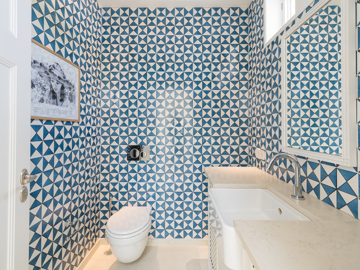 Baño pequeño con azulejos geométricos azules y blancos, sanitario suspendido y lavabo minimalista.