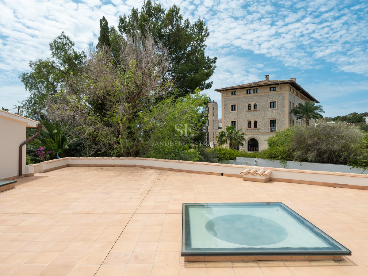 Gran terraza en la azotea con baldosas de terracota, claraboya de cristal y vistas a pinos y una mansión clásica.