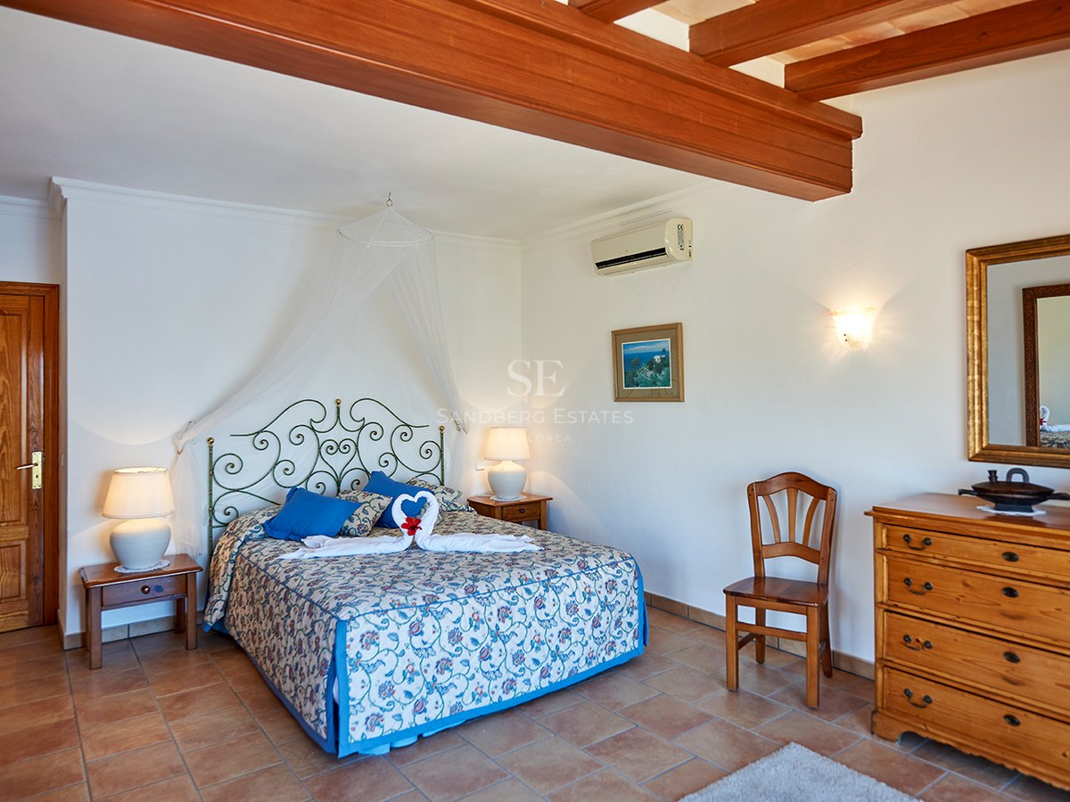 Schlafzimmer mit Terrakottaboden, sichtbaren Holzbalken, Schmiedeeisenbett und klassischen Holzmöbeln.