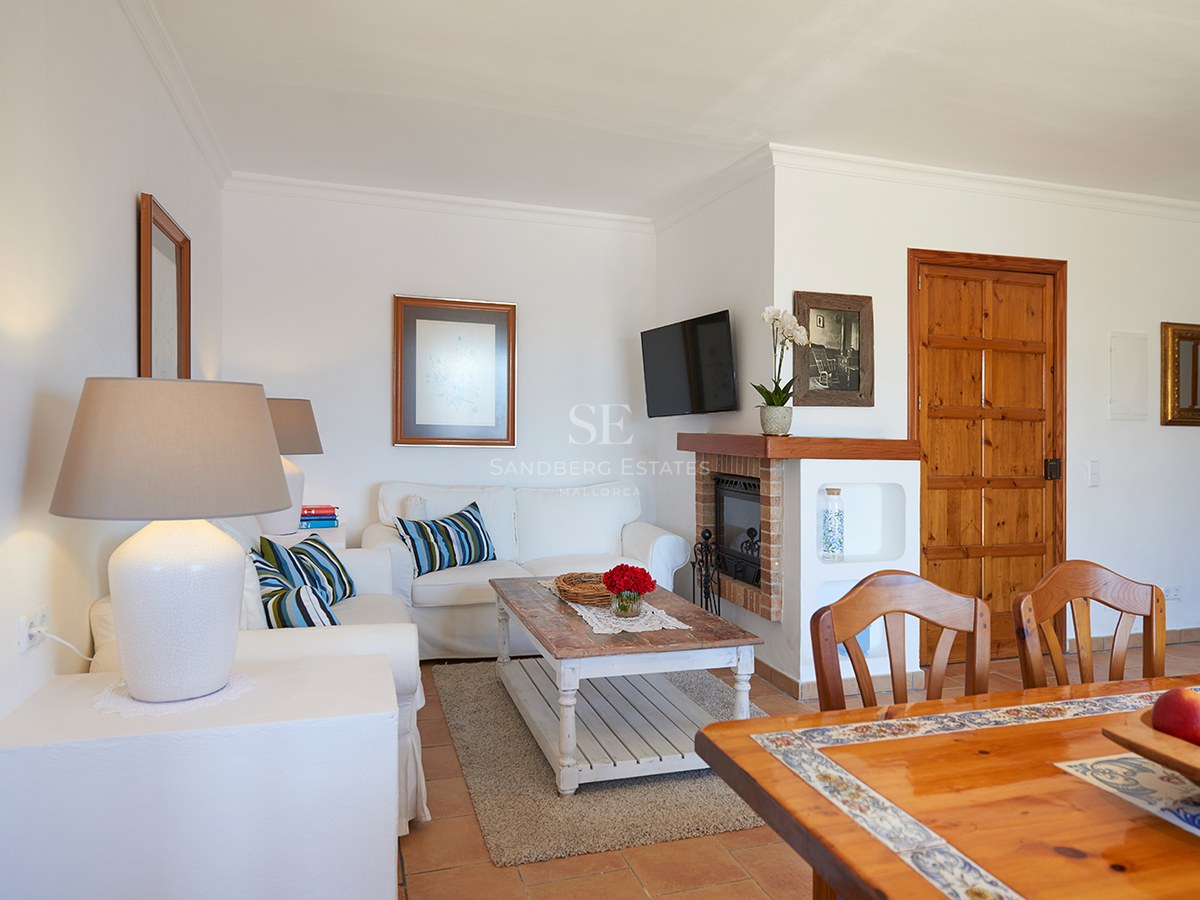 Helles Wohnzimmer mit weißen Sofas, rustikalem Couchtisch aus Holz, Kamin und Terrakottaboden.
