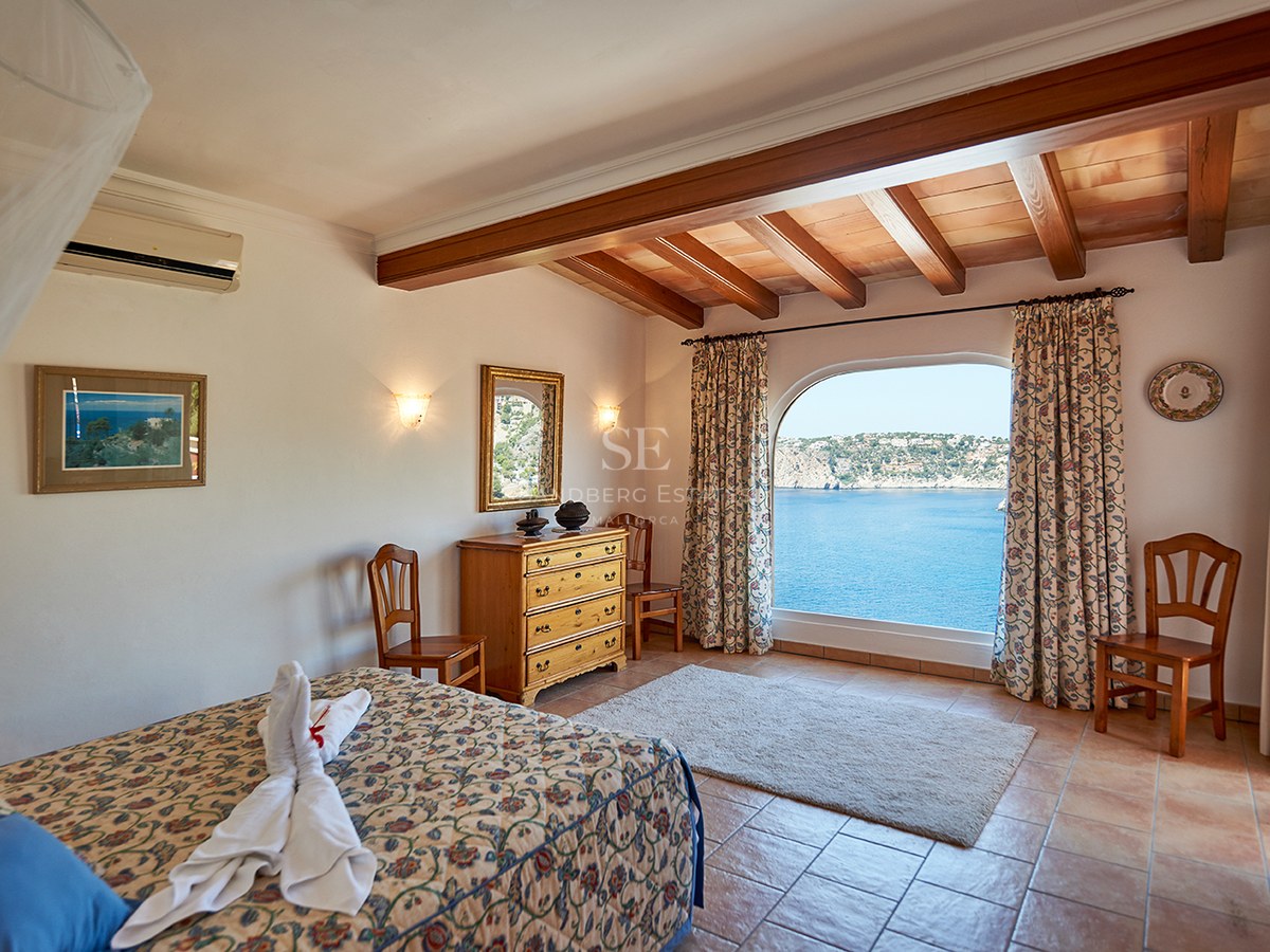 Schlafzimmer mit Terrakottaböden, Holzbalken und einem großen Bogenfenster mit Blick auf das blaue Meer.