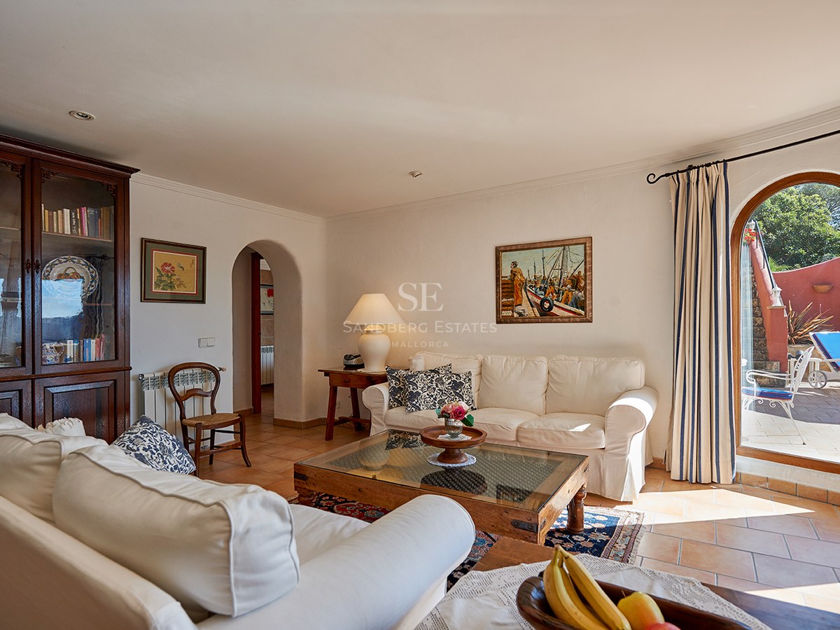 Helles Wohnzimmer mit weißen Sofas, dunklen Holzmöbeln, Terrakottafliesen und einer Bogentür zur Terrasse.