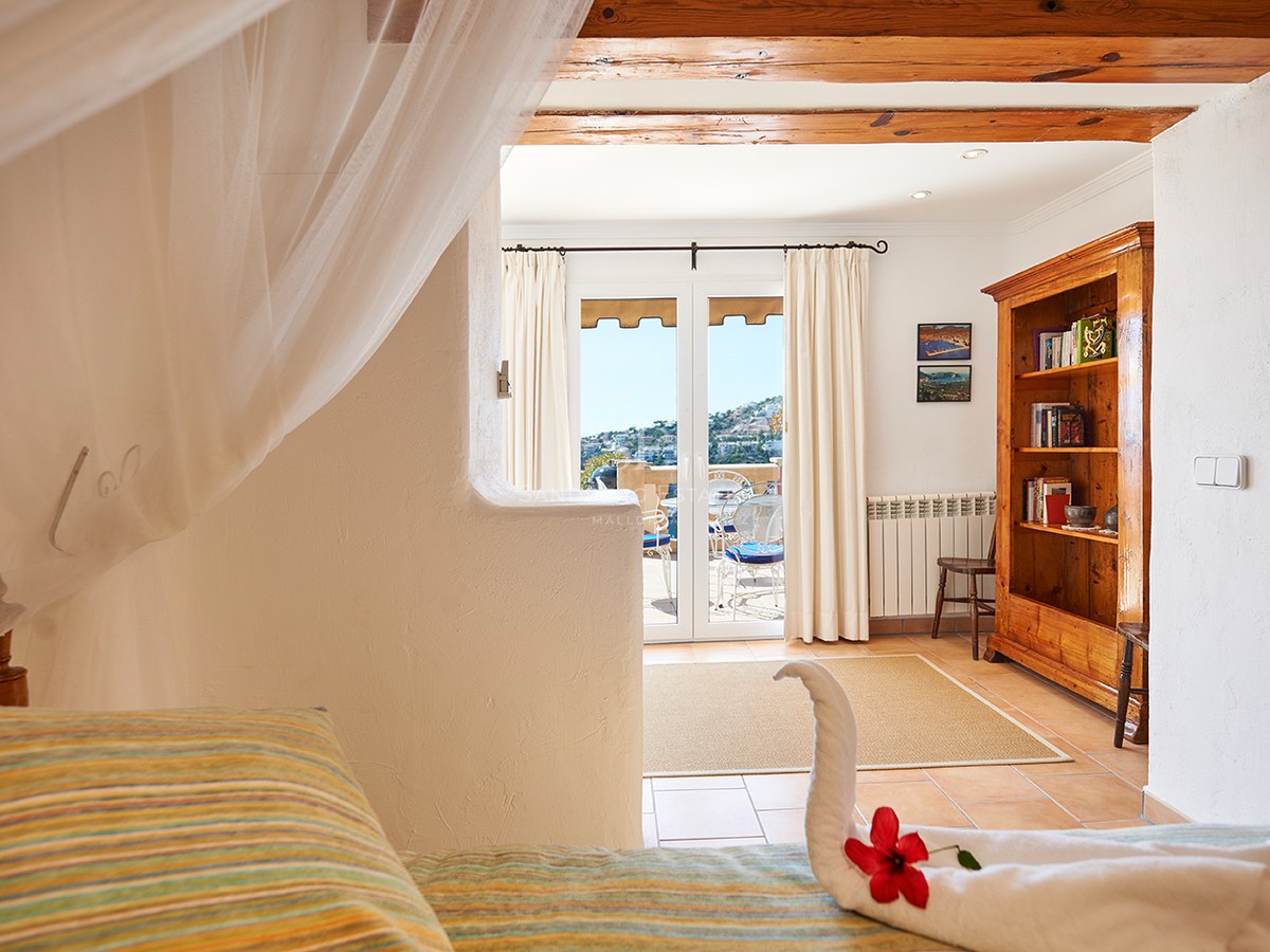 Rustikales Schlafzimmer mit Holzbalken, Himmelbett mit Handtuch-Schwan und Türen zu einer sonnigen Terrasse.