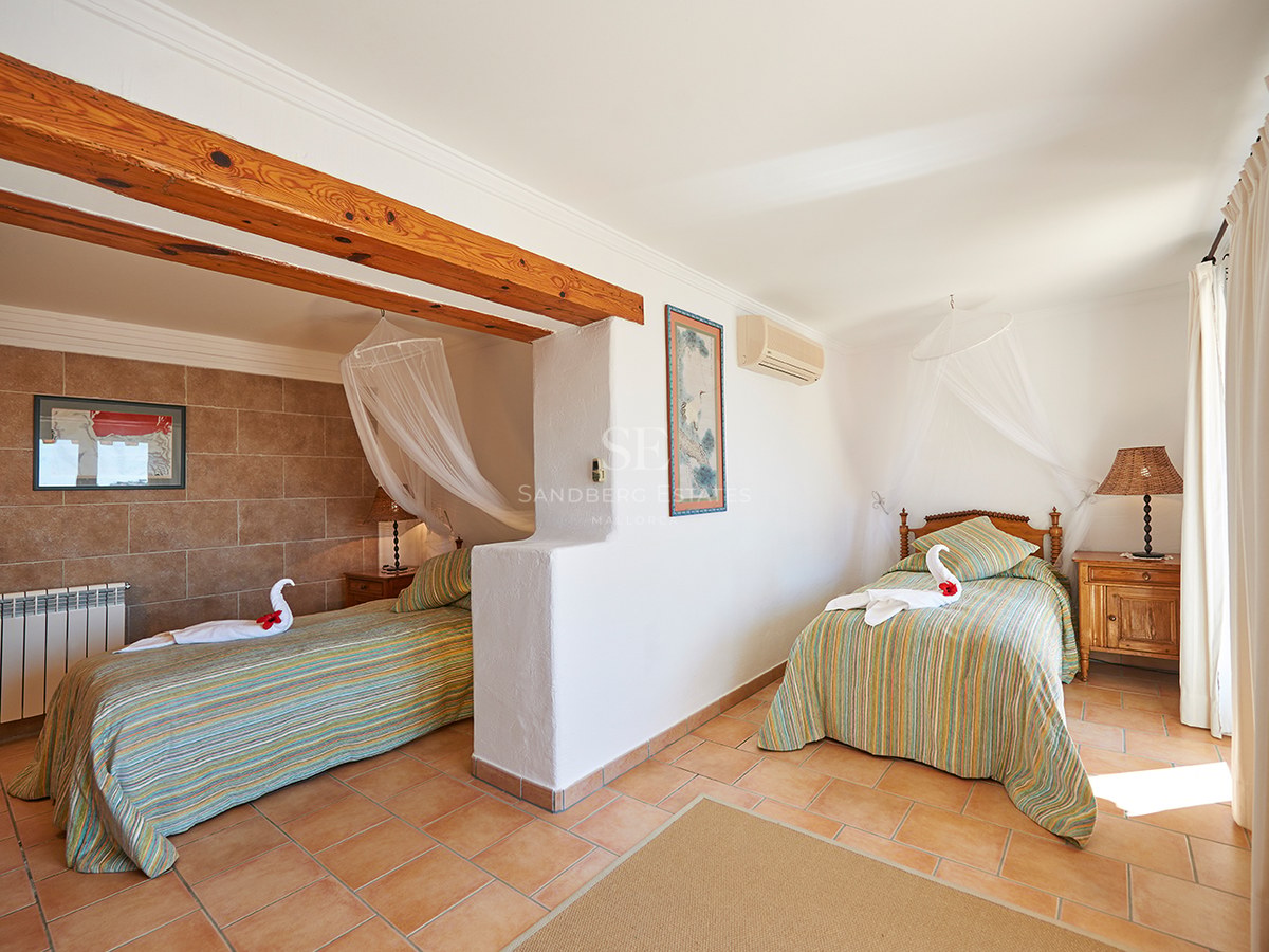 Helles Schlafzimmer mit zwei Einzelbetten, Moskitonetz-Baldachinen, Holzbalken und Terrakottaboden.