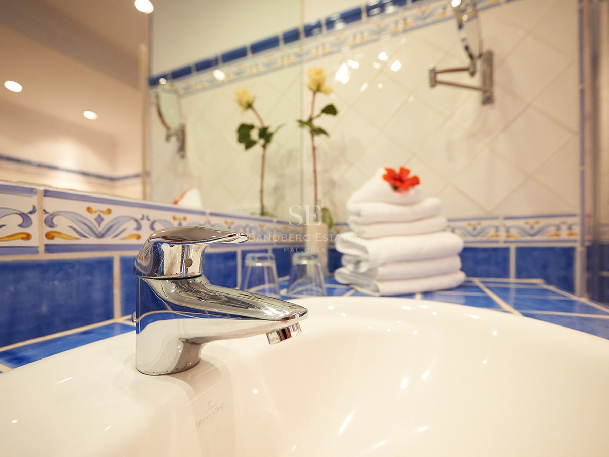 Nahaufnahme eines weißen Porzellanwaschbeckens und verchromten Wasserhahns mit blau gemusterten mediterranen Fliesen.