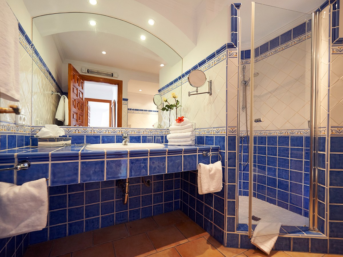 Blau-weiß gefliestes Badezimmer mit einem großen Rundbogenspiegel und einer gläsernen ebenerdigen Dusche.