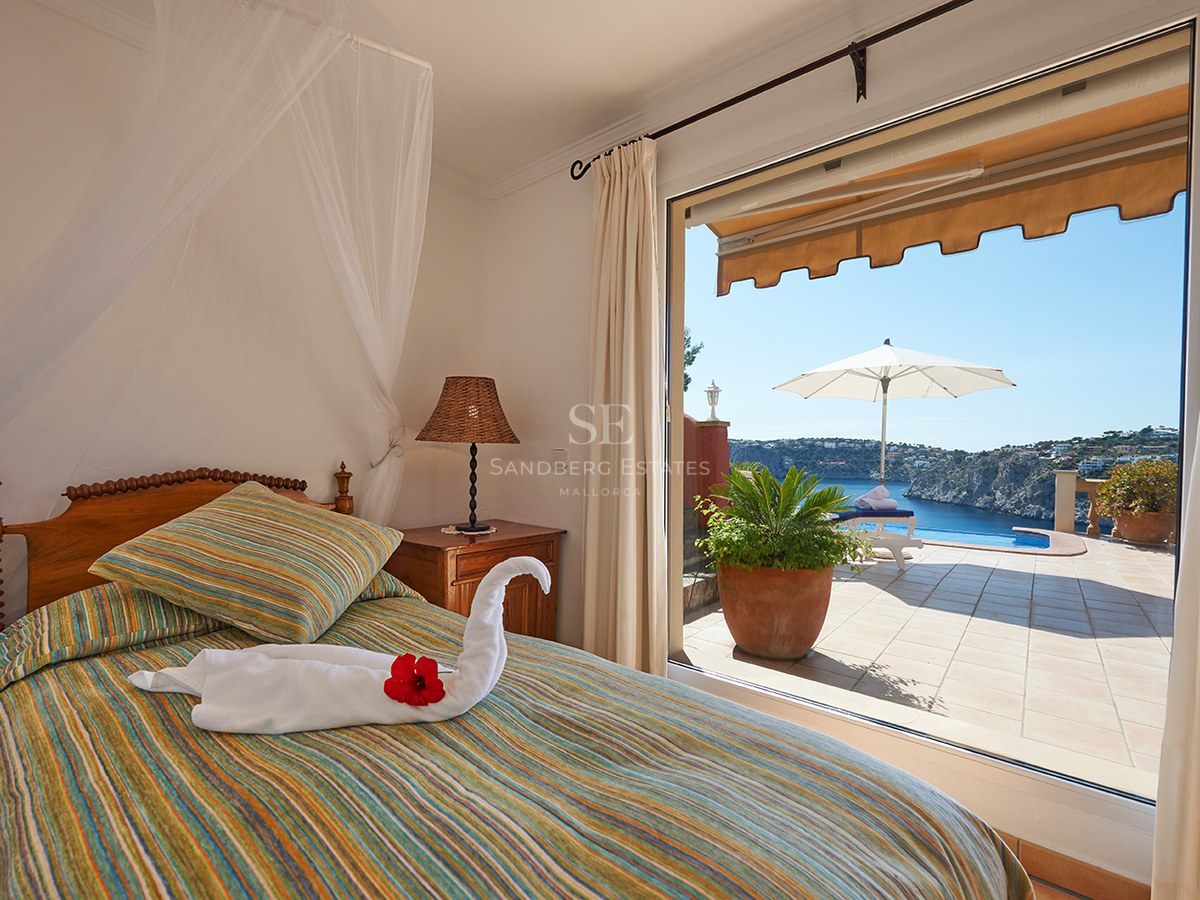 Schlafzimmer mit gestreiftem Bett und Handtuchschwan mit Blick auf eine Terrasse mit Pool und blauem Meer.