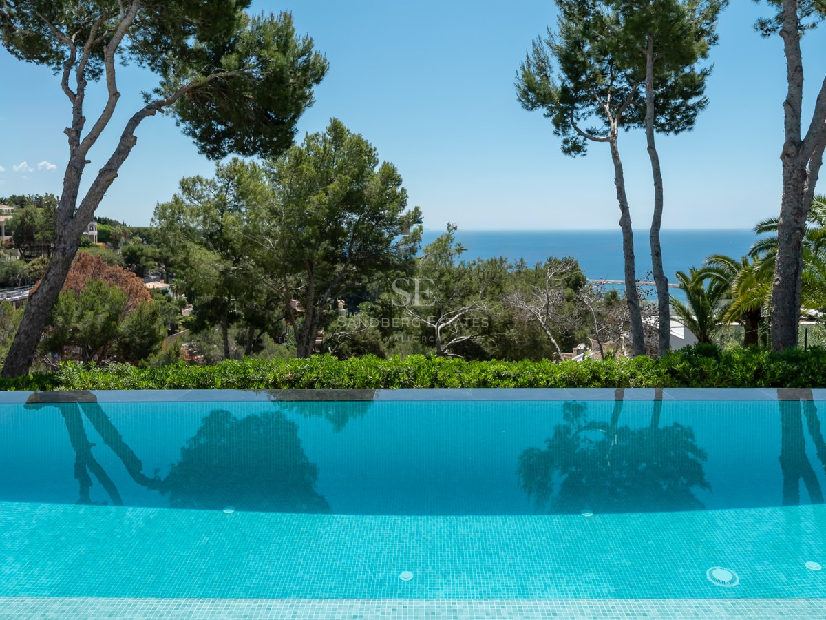 Infinity-pool som speglar tallar, med utsikt över ett grönt landskap och det blå Medelhavet.
