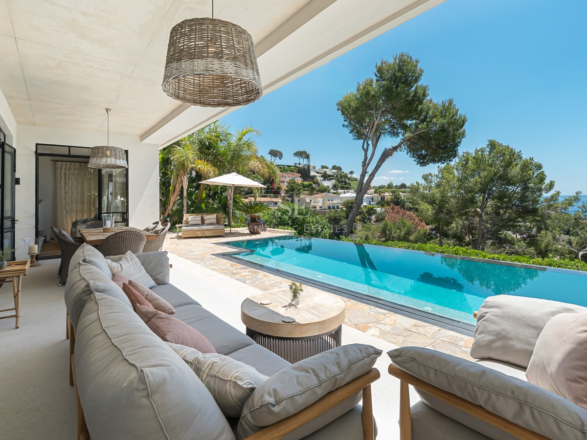 Övertäckt terrass med grå loungemöbler som vetter mot en turkos infinitypool och Medelhavet.