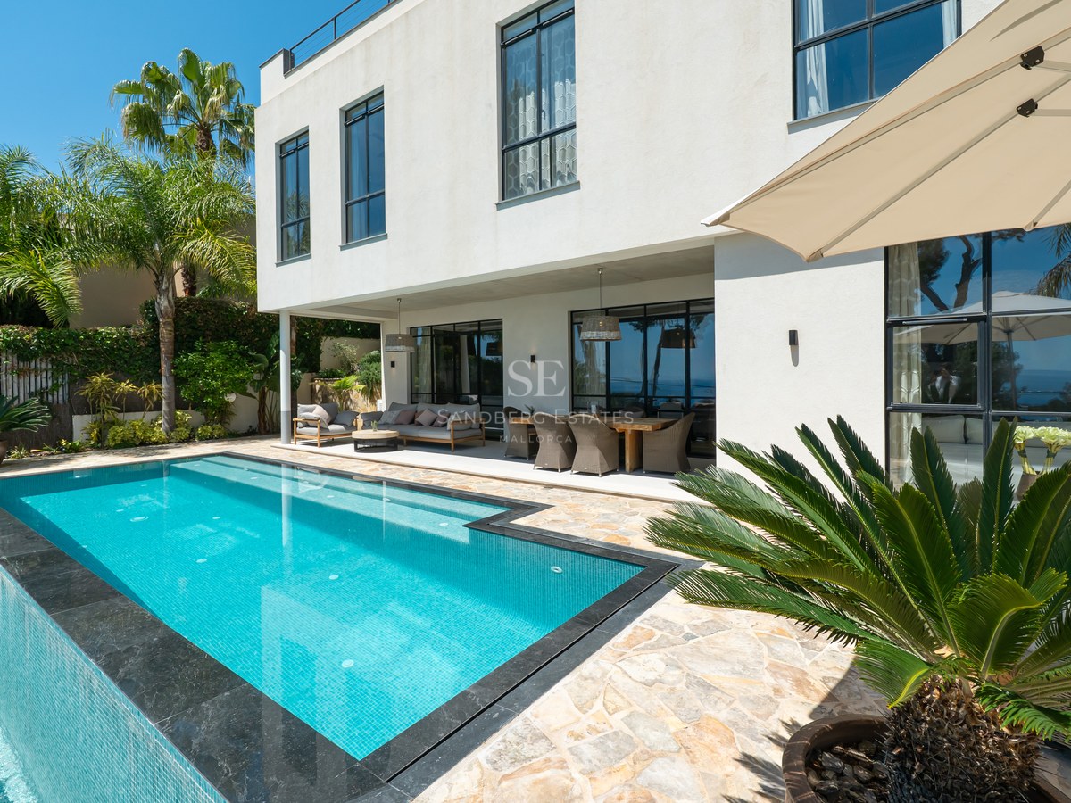 Ljus utomhusscen med turkos pool, täckt terrass och modern vit villa omgiven av palmer.