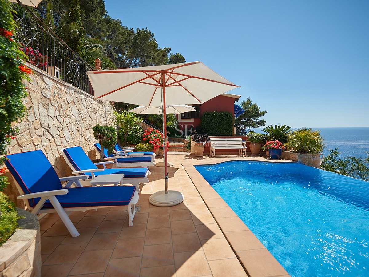 Blå pool på terrass med terrakottaplattor, blå solstolar och vita parasoll med utsikt över Medelhavet.
