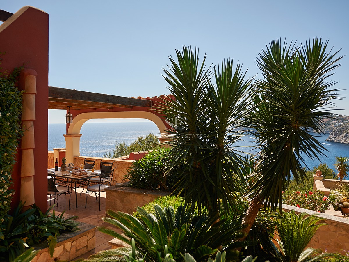 Matplats utomhus på en terrass i terrakotta med bågformad pergola och panoramautsikt över havet.