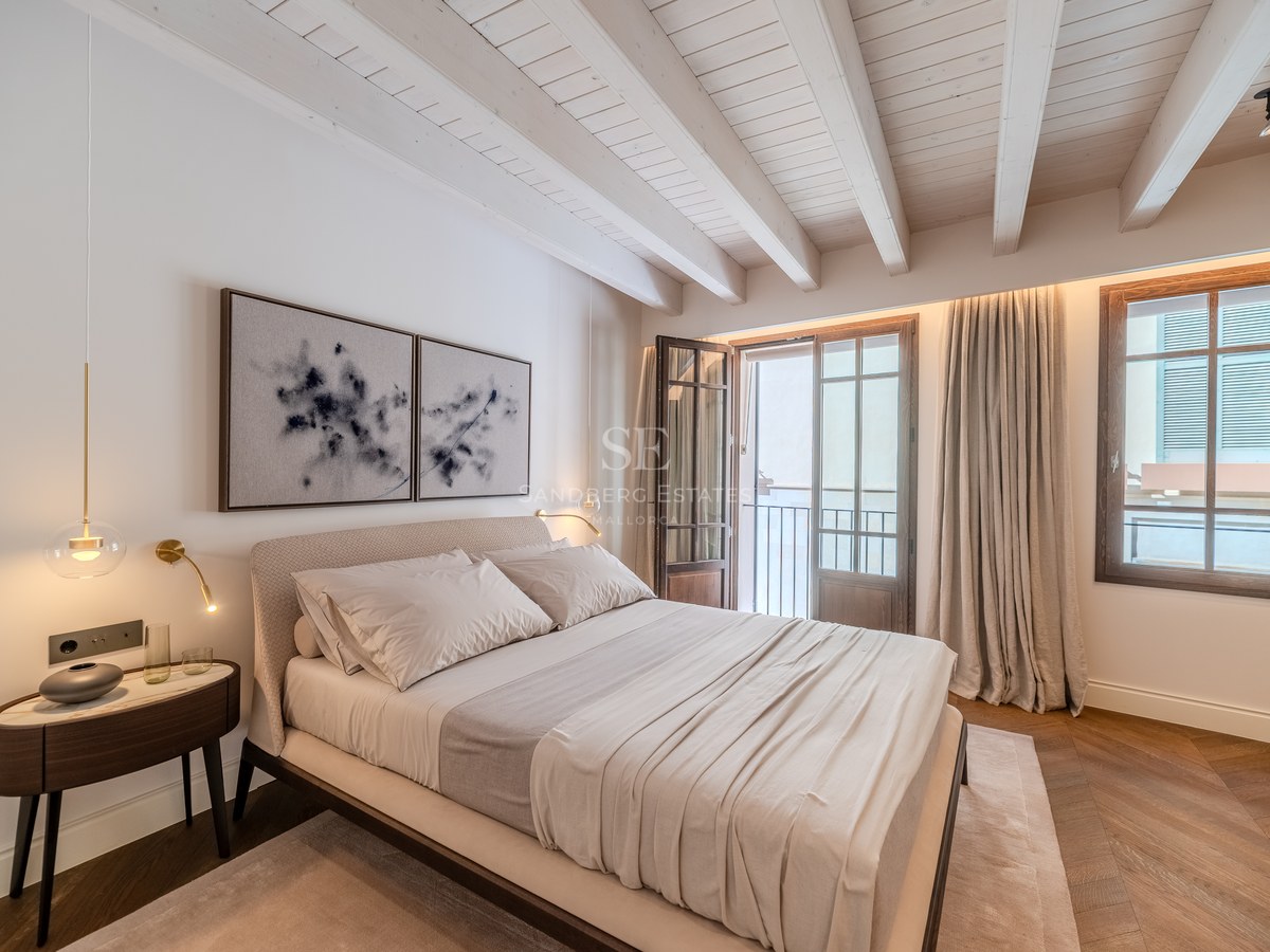 Chambre de luxe avec plafond à poutres blanches, parquet en chevrons, porte-fenêtre et décor neutre.