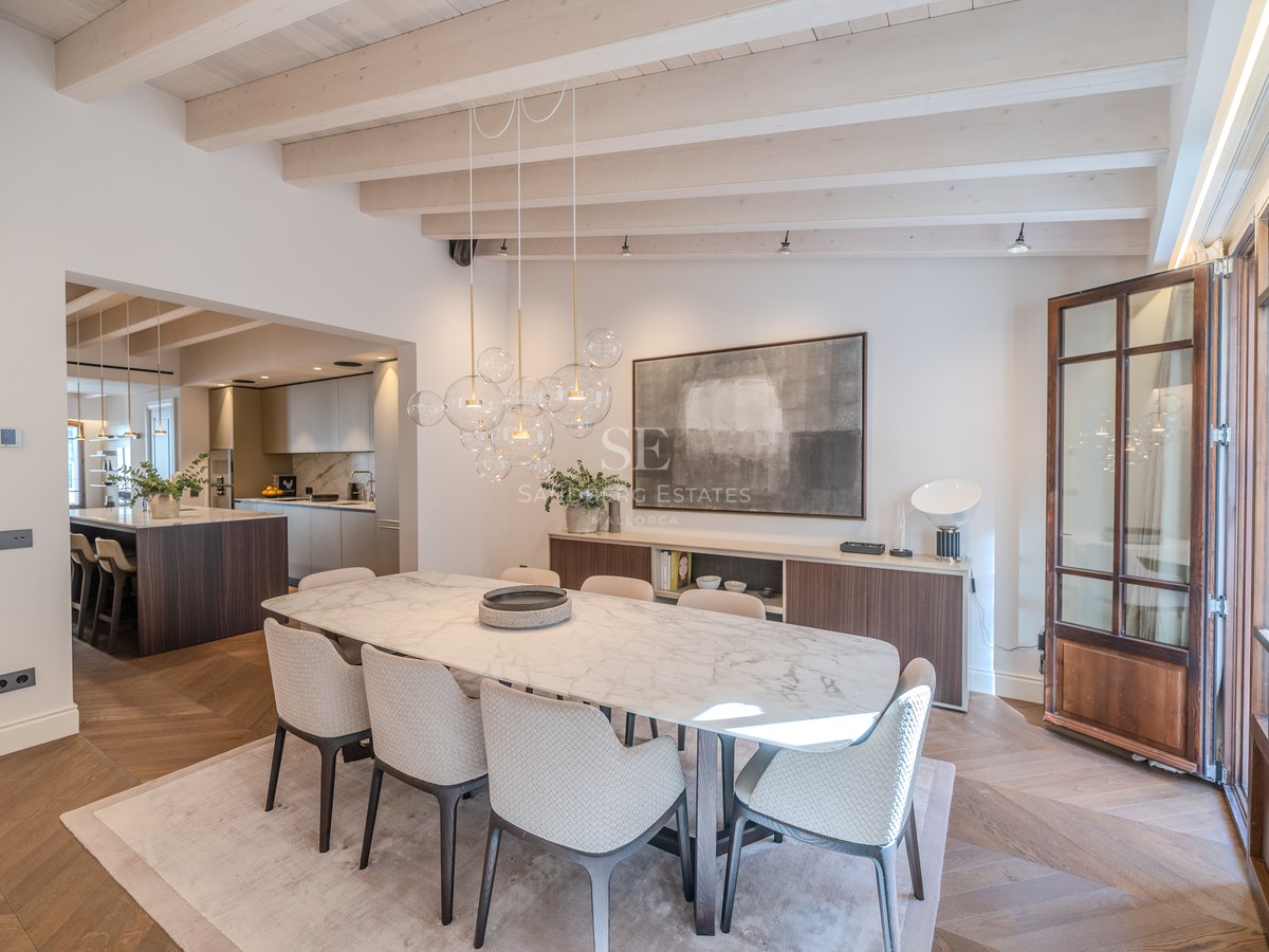 Salle à manger moderne avec table en marbre, lustre designer en verre et poutres apparentes blanchies.