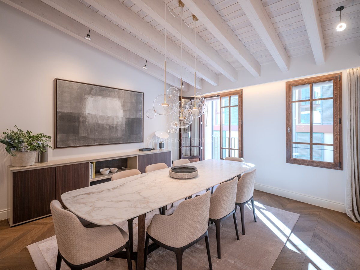 Salle à manger moderne avec table en marbre, chaises texturées, lustre en verre et plafond à poutres apparentes blanches.