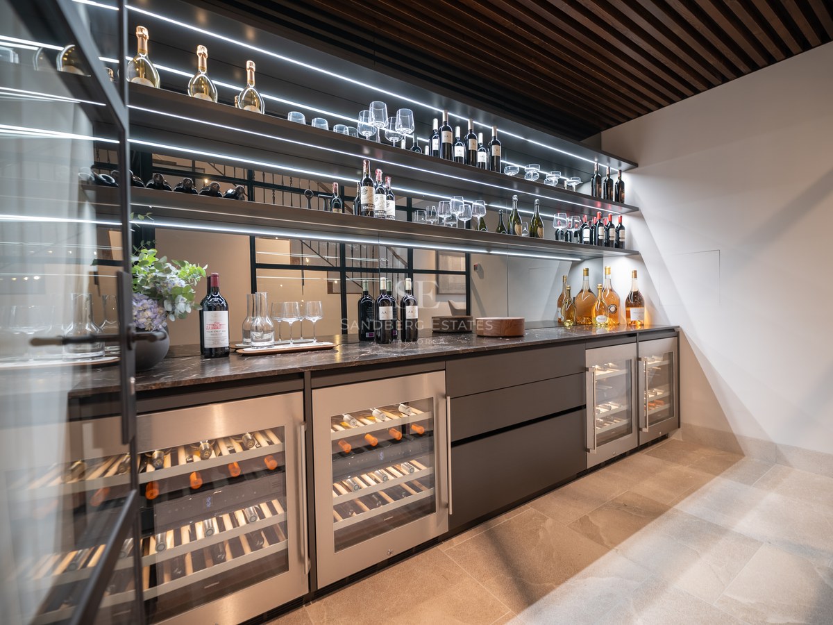 Cave à vin moderne avec refroidisseurs vitrés, étagères rétroéclairées et plans de travail en marbre sombre.