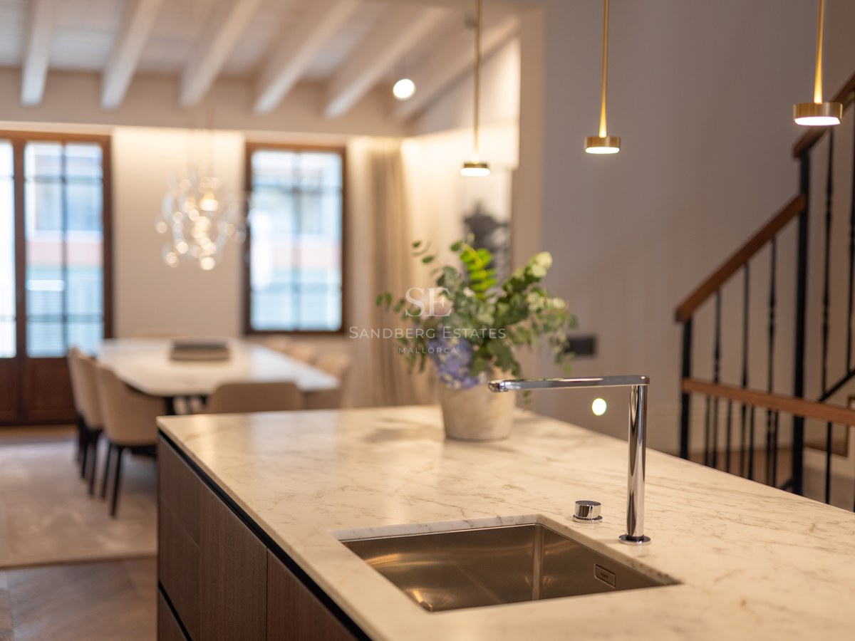 Îlot de cuisine moderne avec comptoir en marbre blanc, robinet chromé et évier intégré, face à la salle à manger.