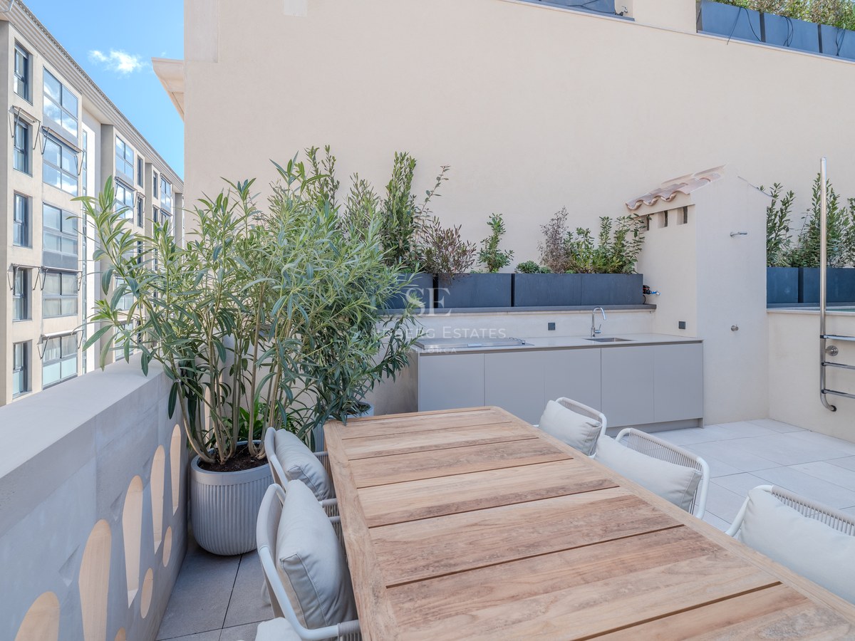 Terrasse moderne sur le toit avec table en bois, kitchenette extérieure et jardinières sous un ciel bleu.