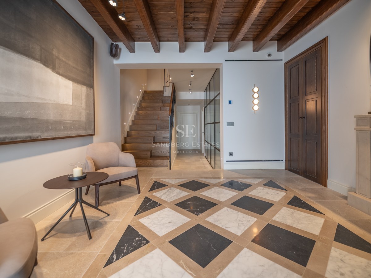 Hall d'entrée de luxe avec sol en marbre géométrique, poutres en bois, escalier en chêne et cheminée en pierre.
