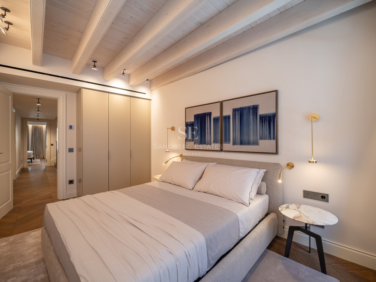 Chambre moderne avec poutres en bois blanchi, armoires encastrées et appliques en laiton.