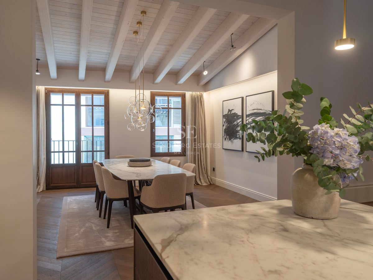 Salle à manger moderne avec table en marbre, chaises rembourrées, plafond à poutres et parquet en chevrons.