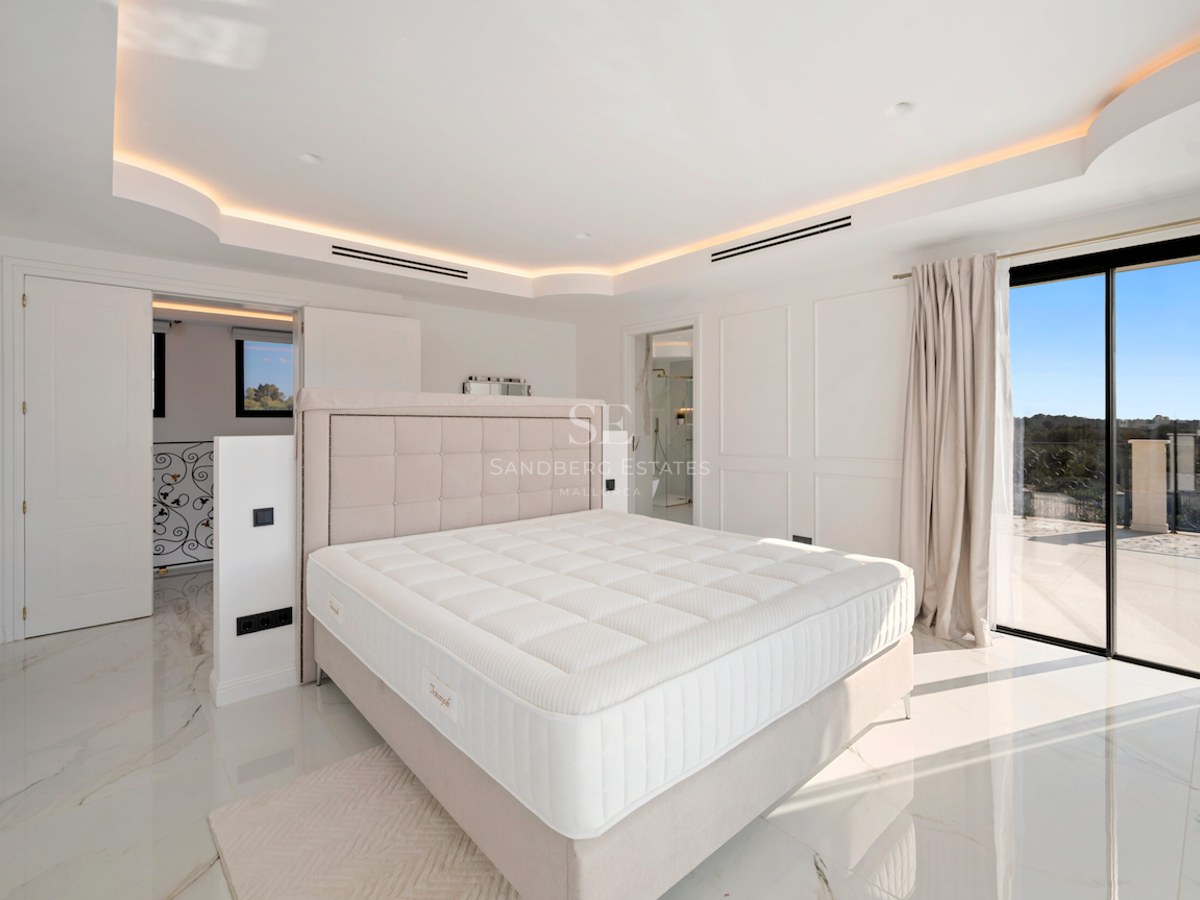 Dormitorio principal luminoso con suelos de mármol pulido, cabecero acolchado, iluminación indirecta y acceso a terraza.