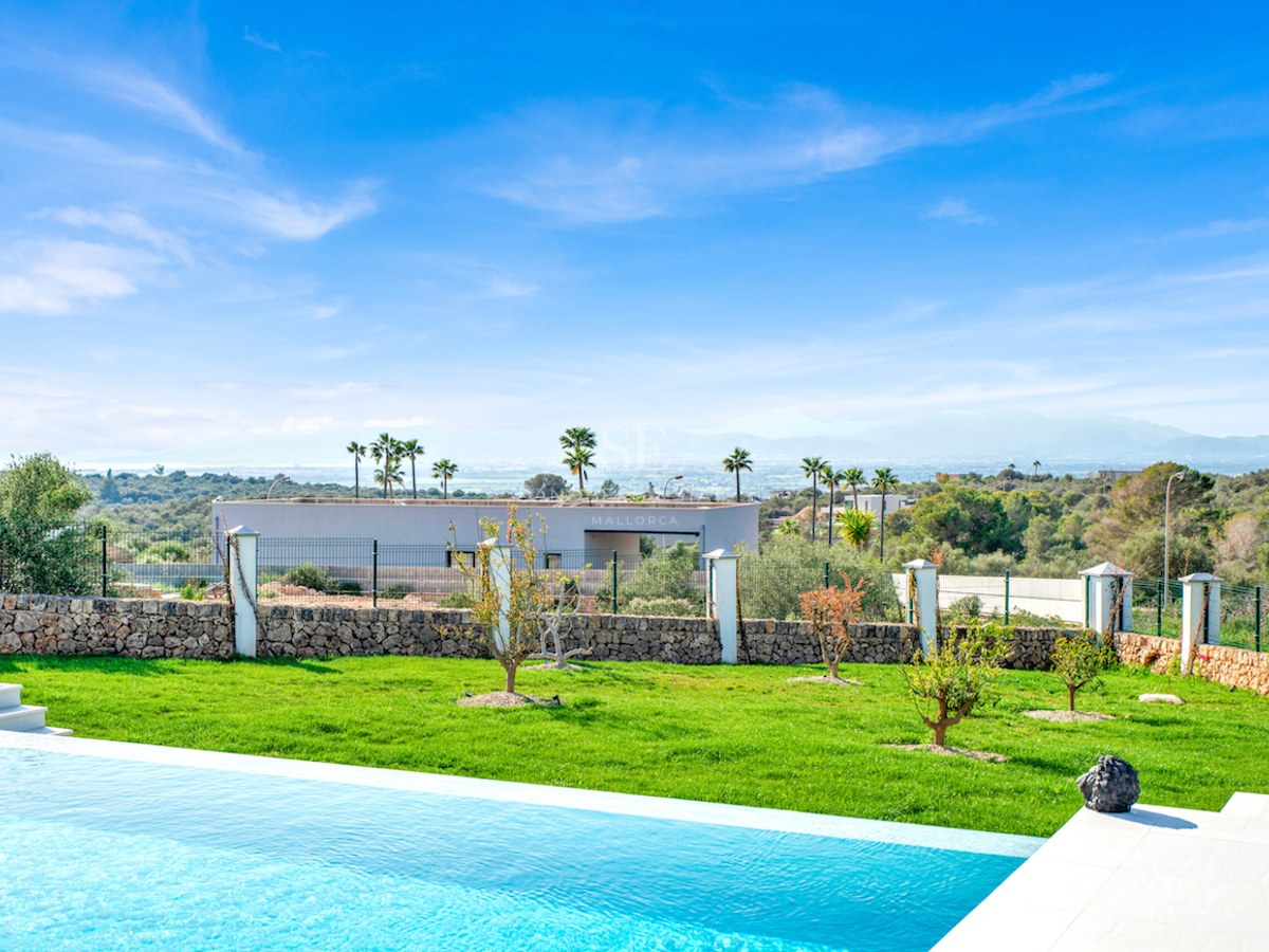 Piscina infinita turquesa y jardín con césped frente a un paisaje de montañas y cielo azul despejado.