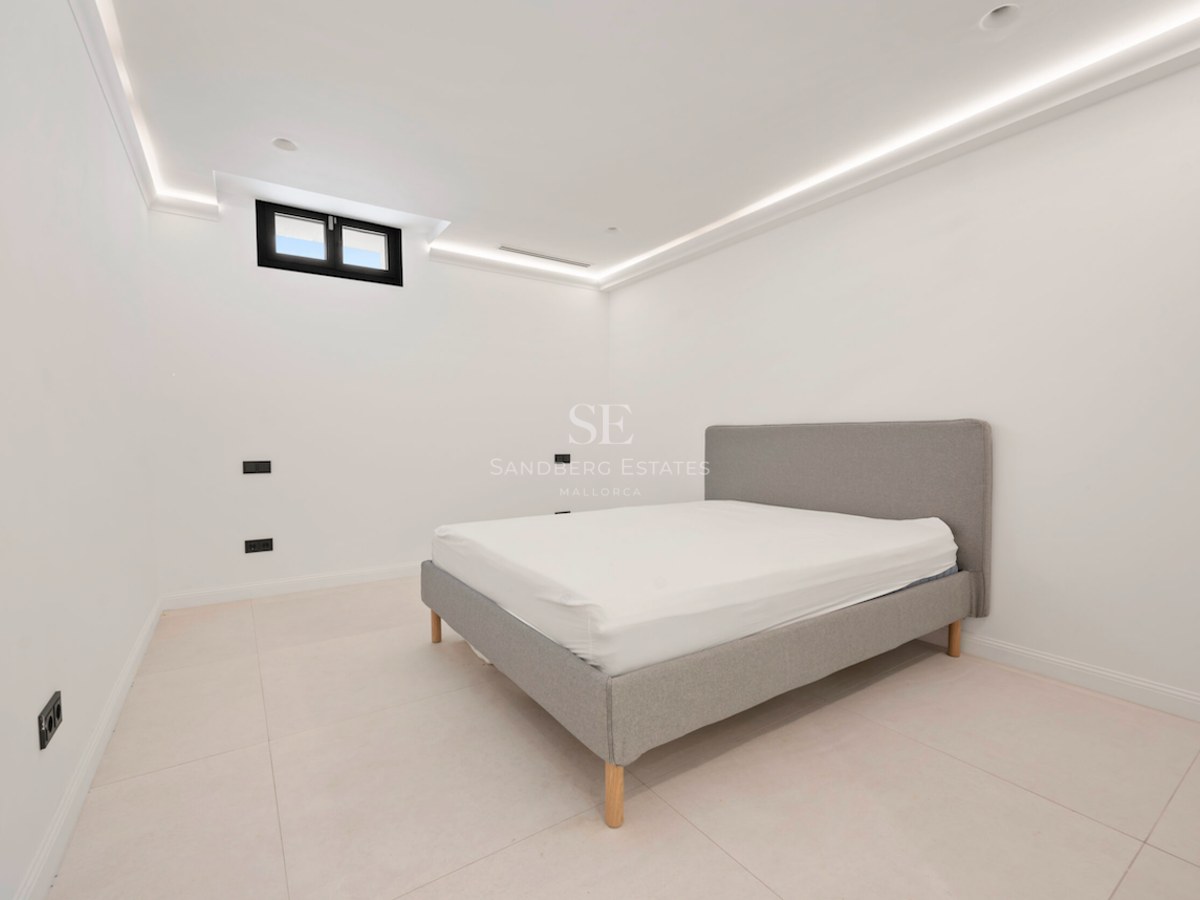 Habitación moderna con cama gris tapizada, suelos de gres claro y foseado de luz LED perimetral en el techo.