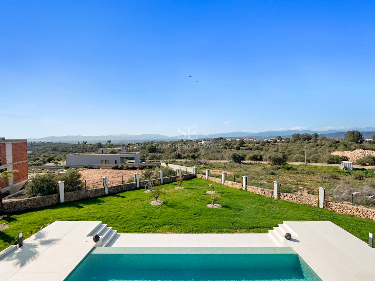 Piscina moderna y jardín de césped con muros de piedra y vistas panorámicas al mar y la montaña.