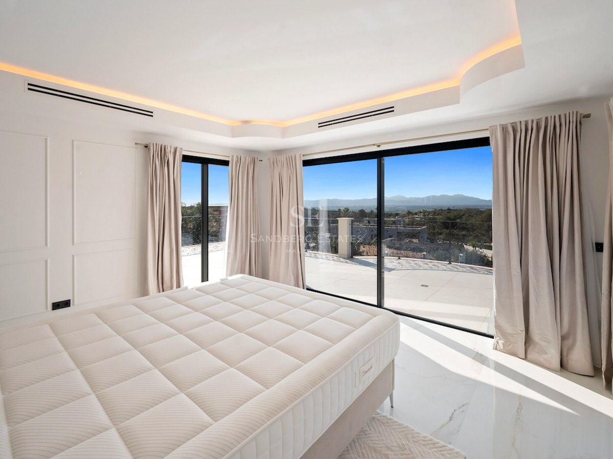 Dormitorio principal moderno con suelo de mármol y ventanales que dan a una terraza con vistas a la montaña.